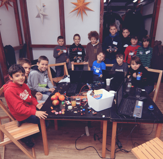 Children around a workshop table with fruit, electronics and a laptop